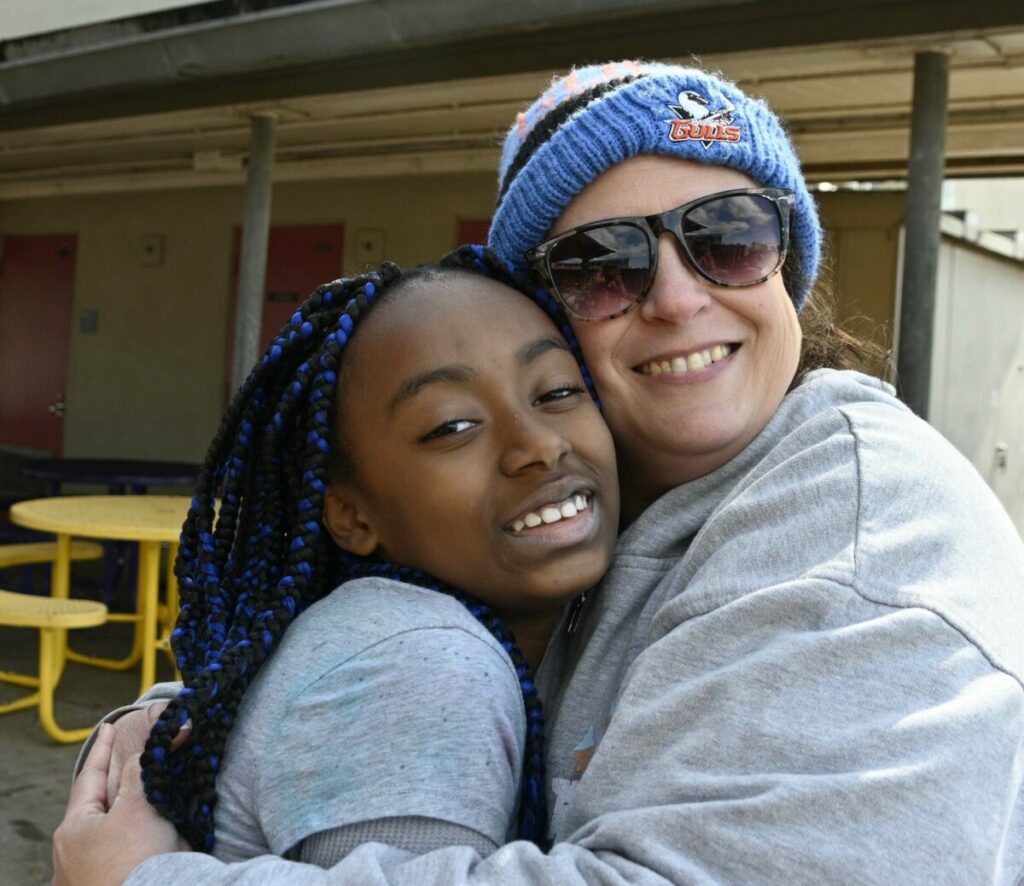 San Diego tuition-free Cooperative Charter School student hugging teacher with the school building in the background