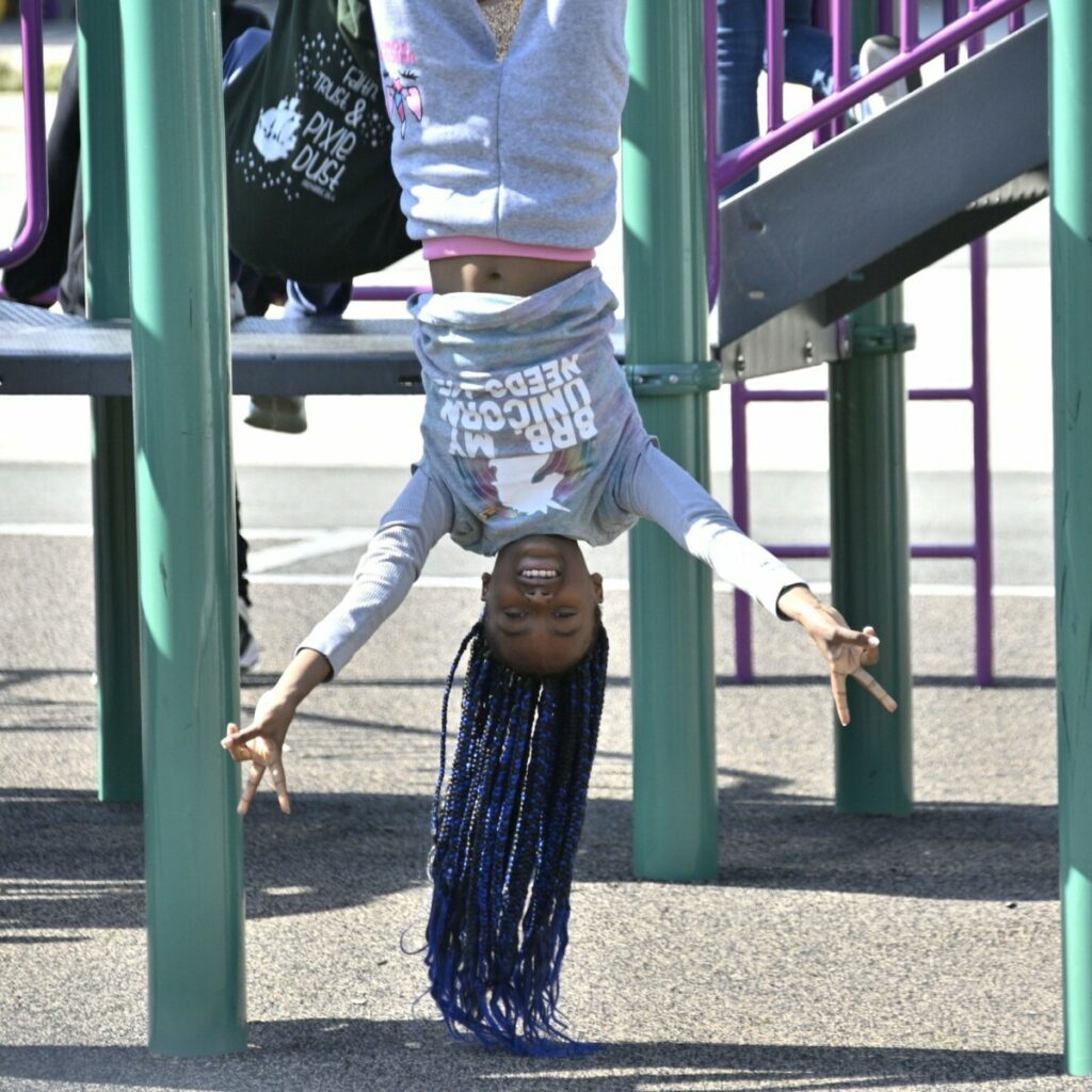 Student at San Diego Cooperative Charter School hanging upside down on playground.