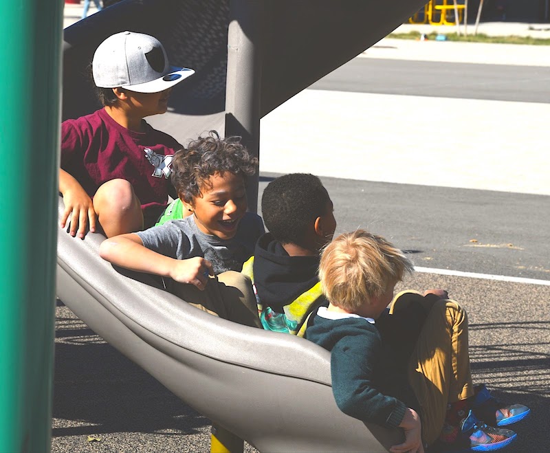 four students at tuition-free San Diego Cooperative Charter School going down playground slide together